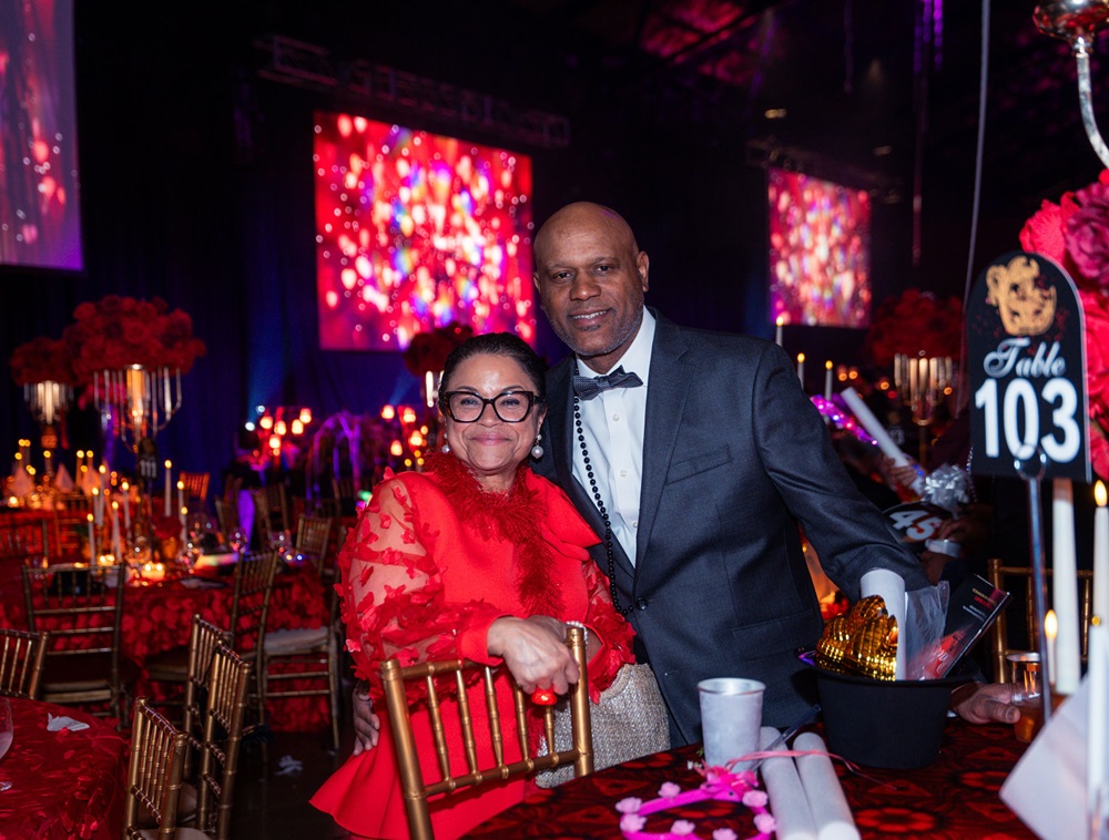 Smiling couple posing together next to Table 103.